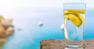 a refreshing glass of sparkling water with lemon slices against a seaside backdrop, ideal for hydration and healthy living