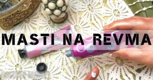 a hand holding a tube of pink hand cream labeled "Revma" with a decorative cap, placed on a patterned cloth.