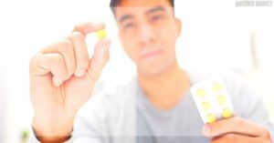 a hand holding a small yellow-green pill and a blister pack of similar pills, likely for joint-related medication research.